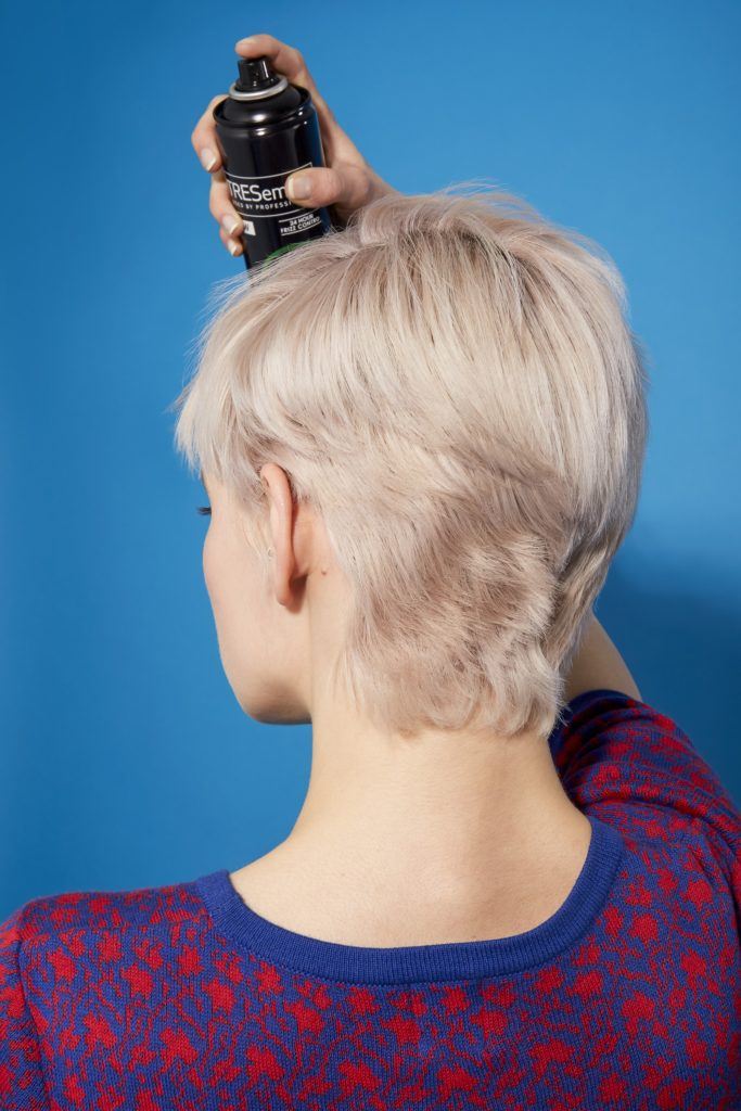 back view of a woman with platinum blonde hair in a pixie cut style using hairspray to set her style in place