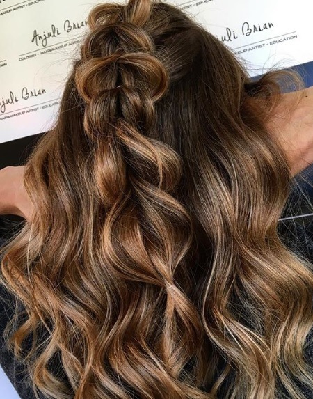 Summer hair colours: Back view of a woman with warm brunette curly long hair in a half-up pull-through braid