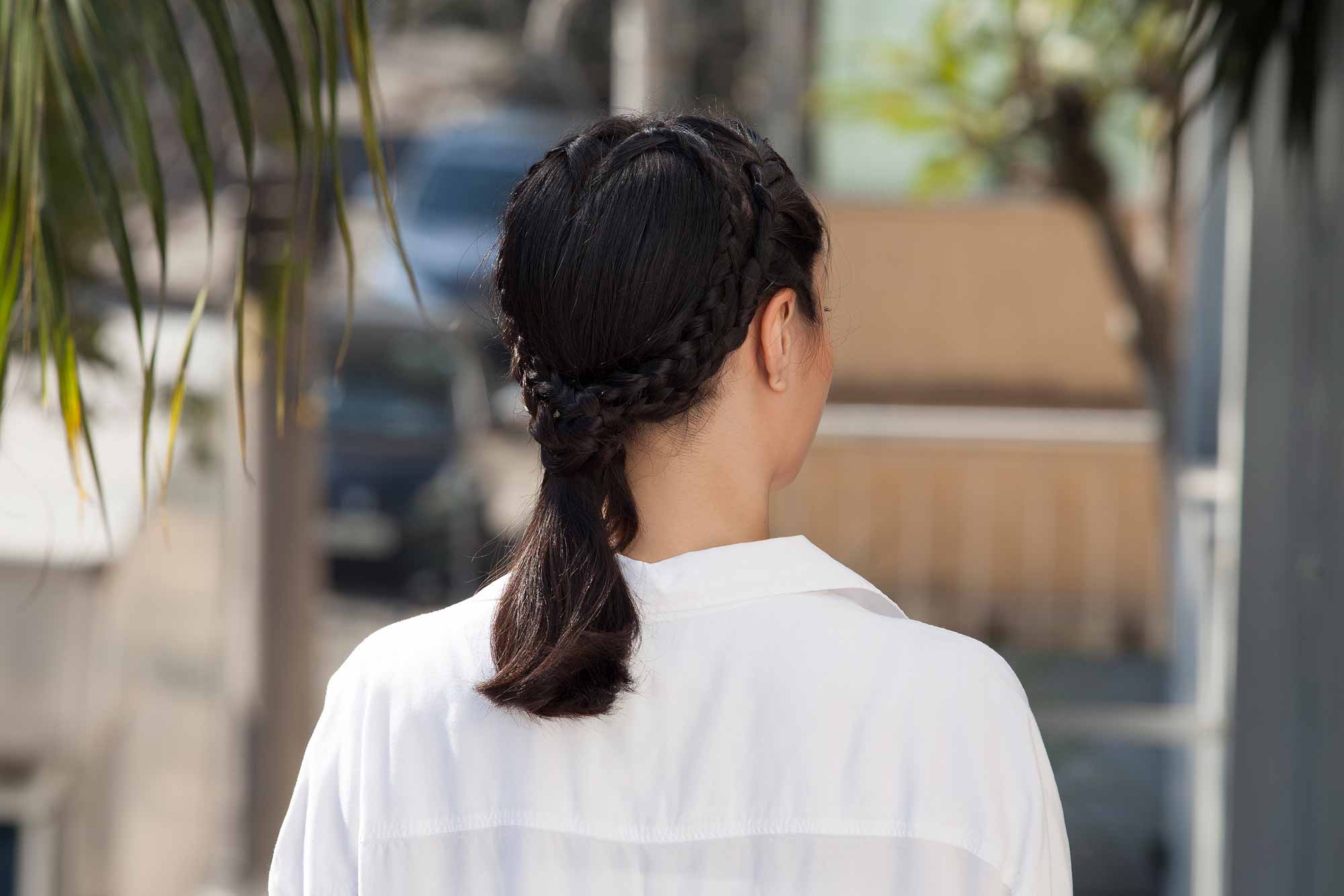 close up shot of model with heart braid ponytail hairstyle, wearing white blouse and posing outside
