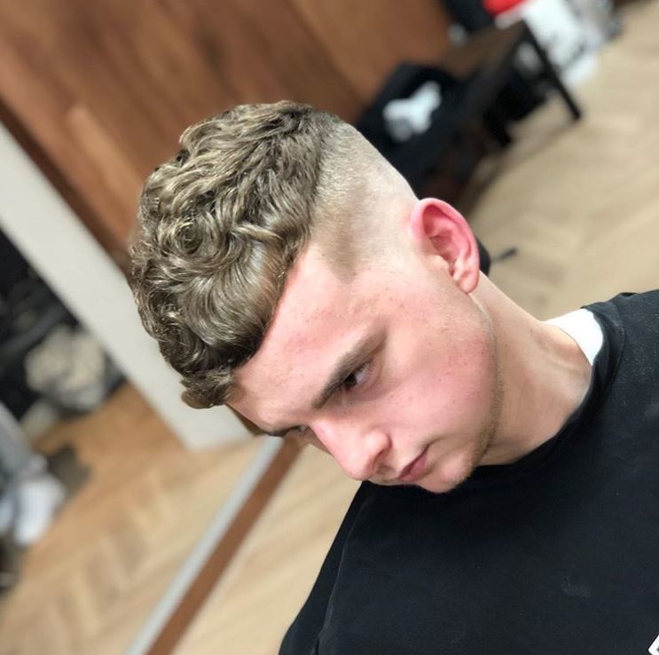 close up shot of a man in barber shop with dark blonde curly hair undercut style