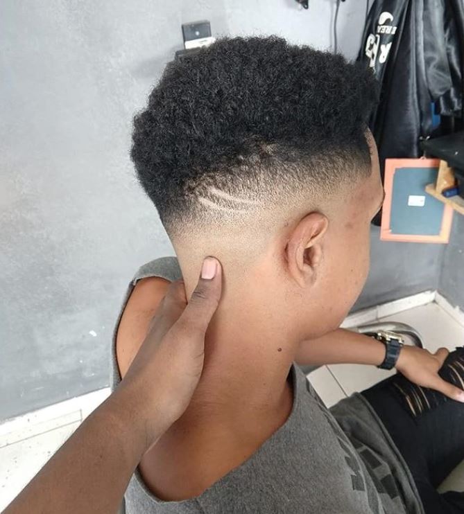 close up shot of a man in barber chair with naturally curly hair undercut, complete with shaved line design on the side