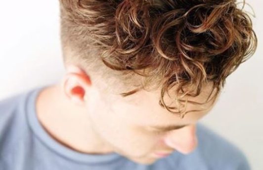 male with hair styled in large loose brown curly hair undercut