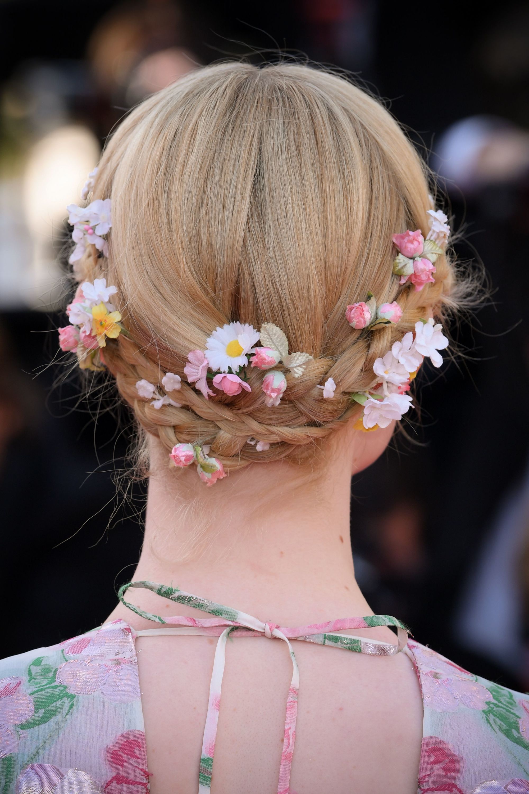 Elle Fanning with her golden blonde hair styled into a low double braided updo with flowers weaved through it
