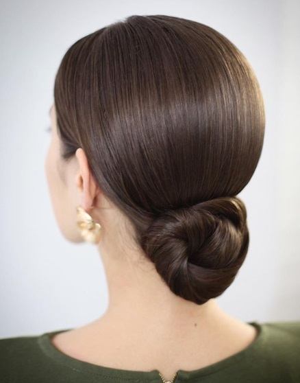 Wedding updos: Back view of a brunette with a sleek low twisted bun, wearing statement earrings