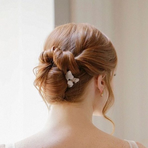 Wedding updos: Back view of a redhead with a knotted updo with flower hair accessory and loose strands around her face