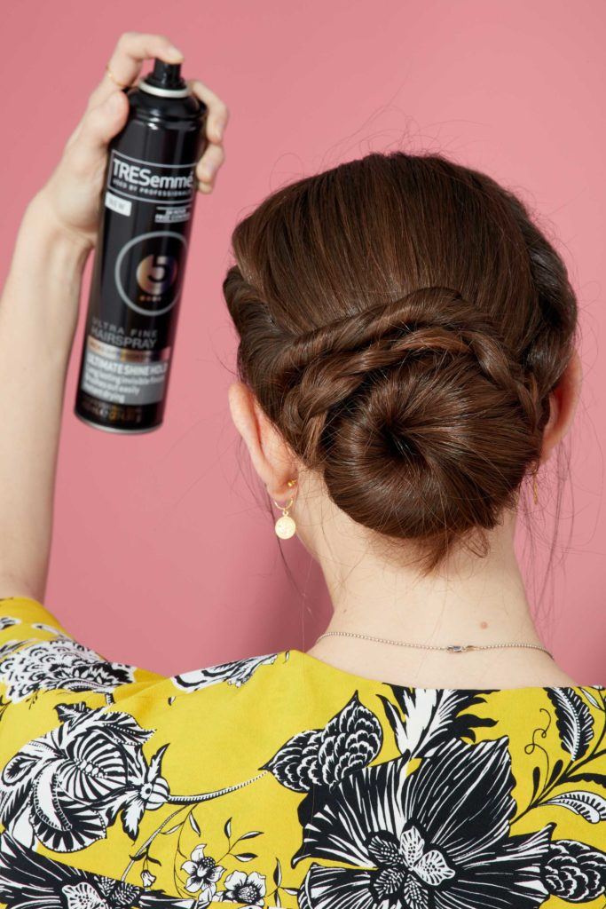 view from behind of a brunette model with her hair in a french braided bun spraying it with tresemme hairspray