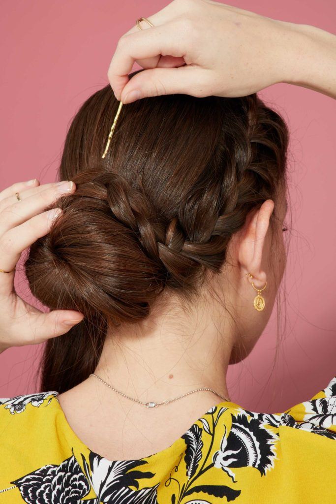 close up view from behind of a brunette model wrapping a french braid around a bun and pinning with a bobby pin