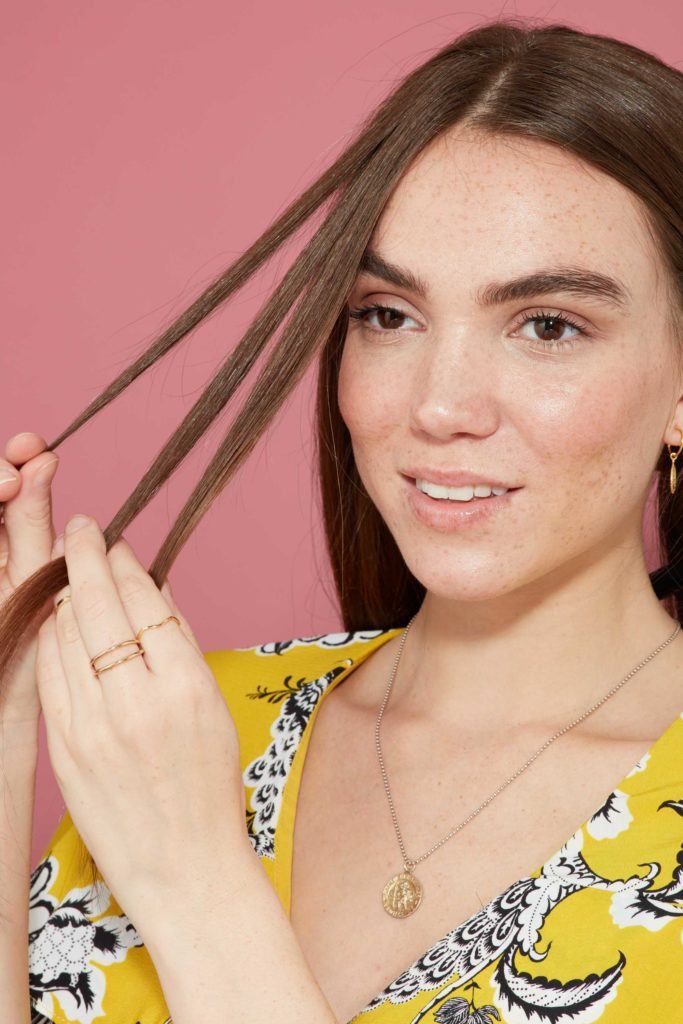close up of a brunette model holding three pieces of hair about to start braiding her hair