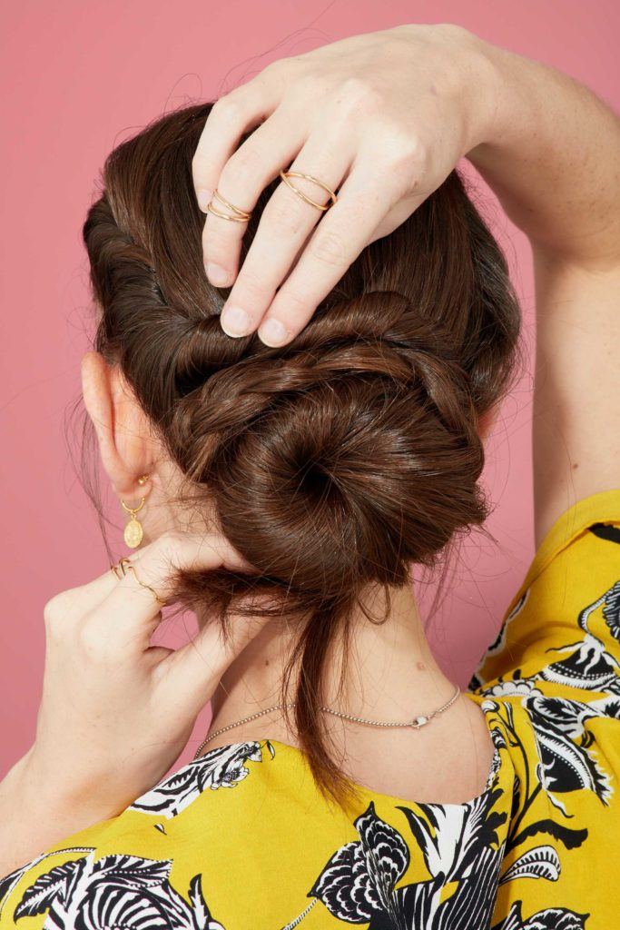 close up view from behind of a brunette model twisting the front section of her hair and wrapping it around a bun