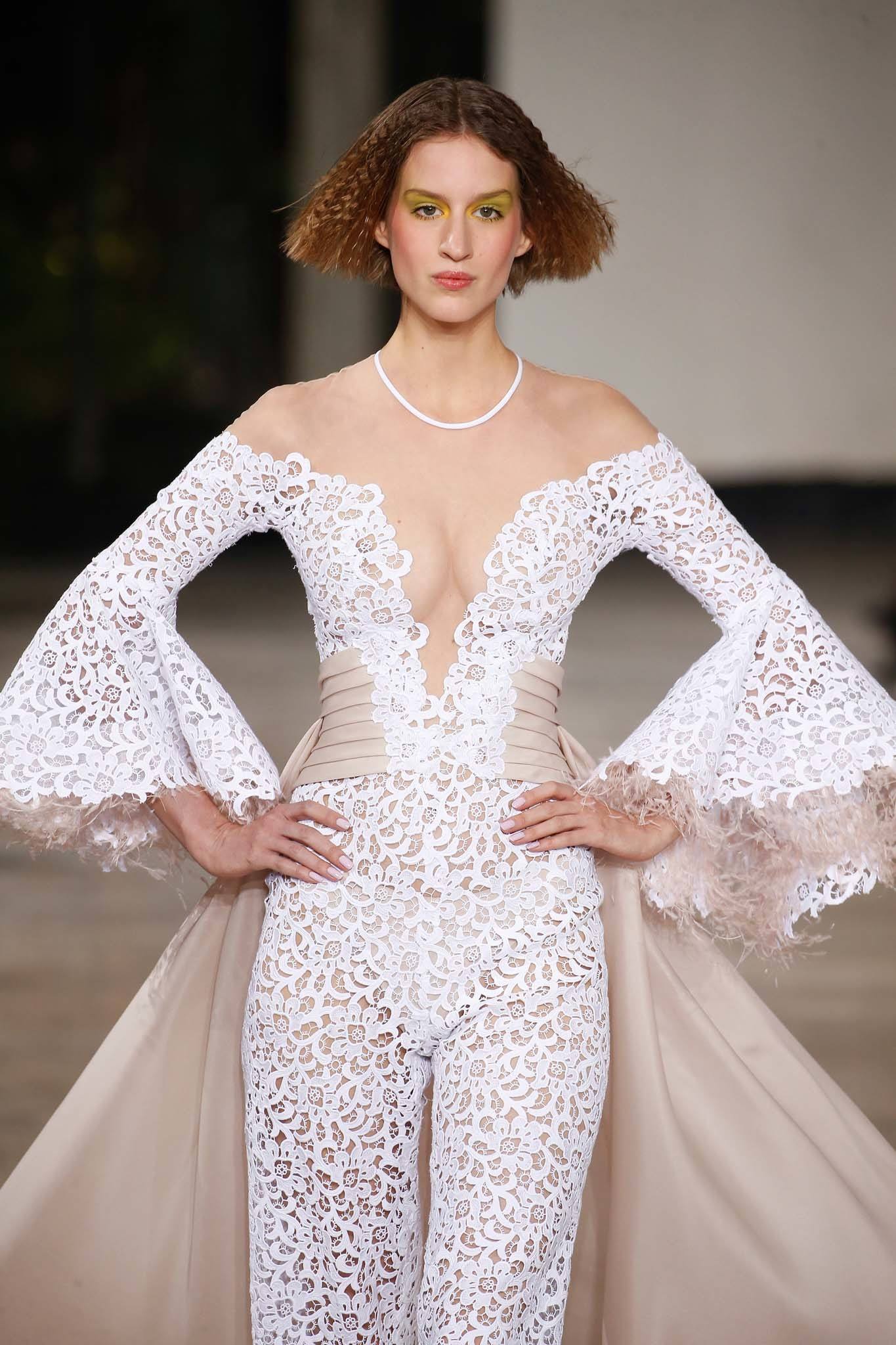 Haute Couture: Model with short crimped brown bob on the Georges Chakra SS19 runway in white lace detail jumpsuit with skirt.