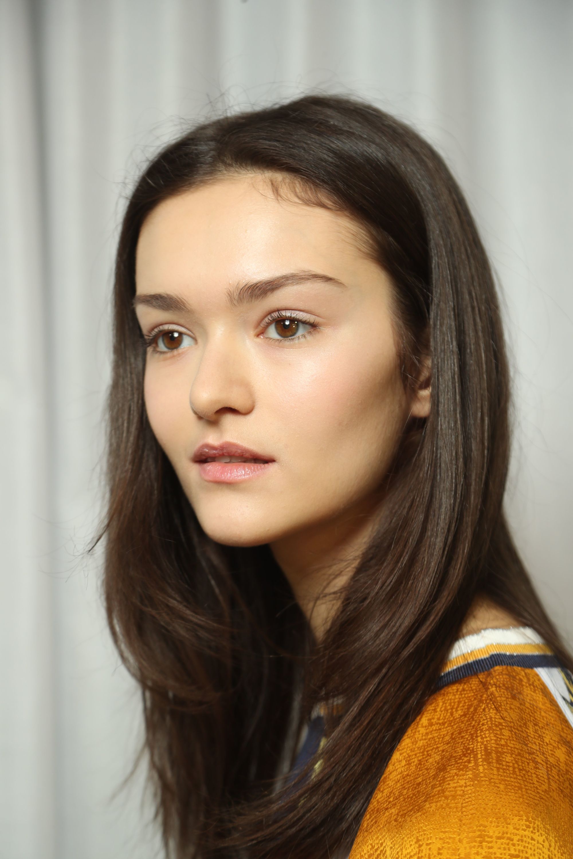 Haircuts for thick hair: Close up behind the scenes fashion week photo of a brunette model with sleek long hair with layers
