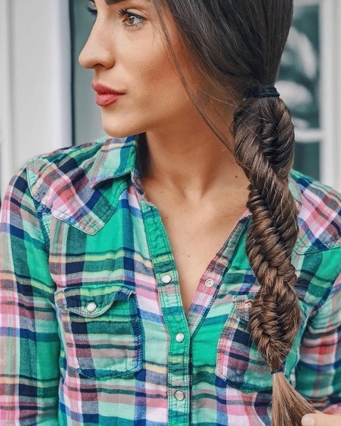 Close up shot of a woman with long brunette hair in a side braided DNA braid, wearing a green and pink plaid shirt.