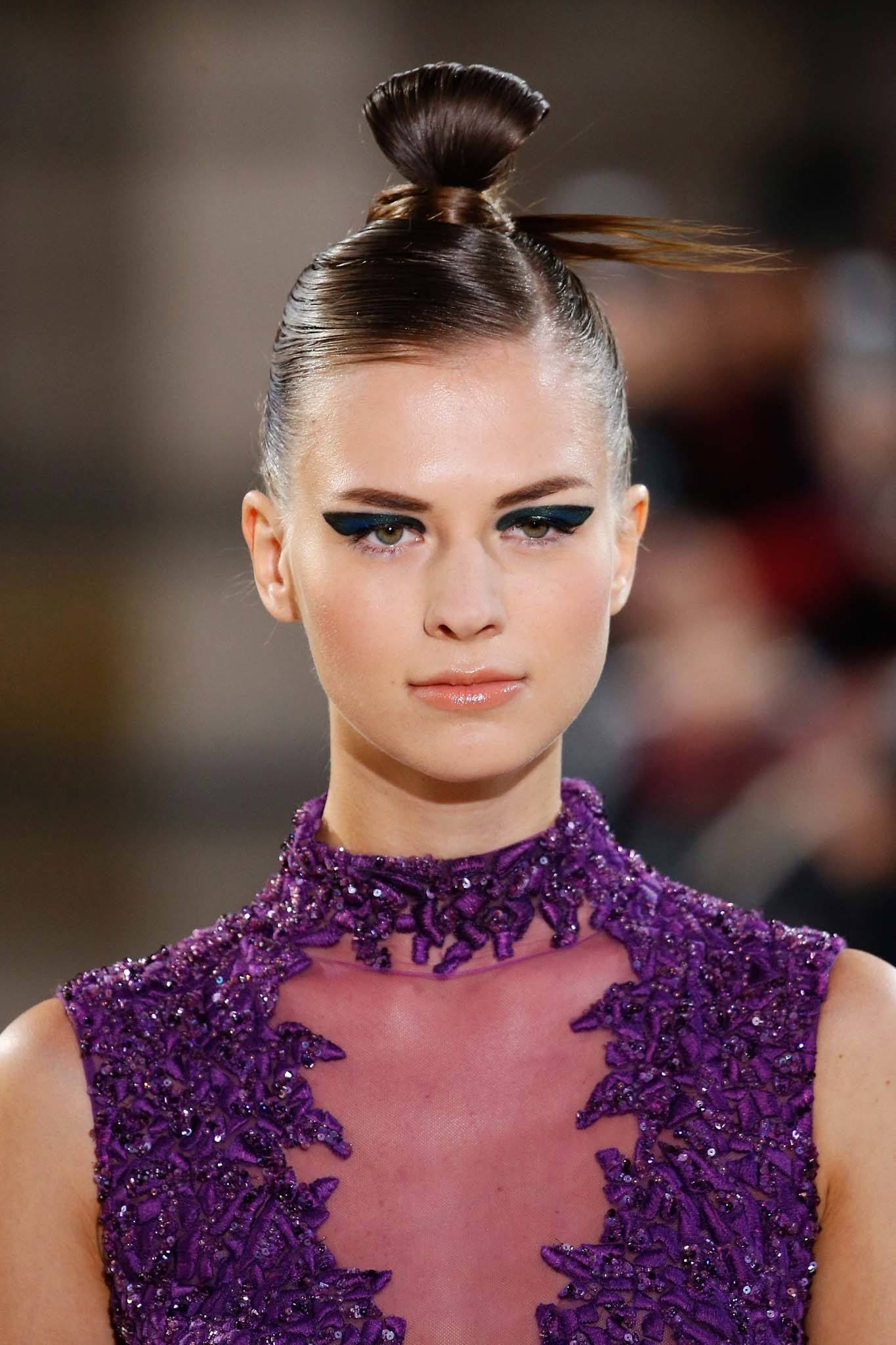 Haute Couture: Model with brown hair in high twisted ninja bun with dark winged eyeliner and a purple dress on Tony Ward SS19 runway.