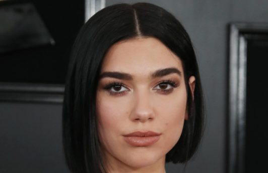 Red carpet hairstyles: Dua Lipa with dark brown straight blunt bob on red carpet wearing a strapless pale blue dress and diamond necklace.