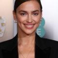 Red carpet hairstyles: Irina Shayk with brown hair styled in side parted smooth bun updo wearing a black smart jacket.