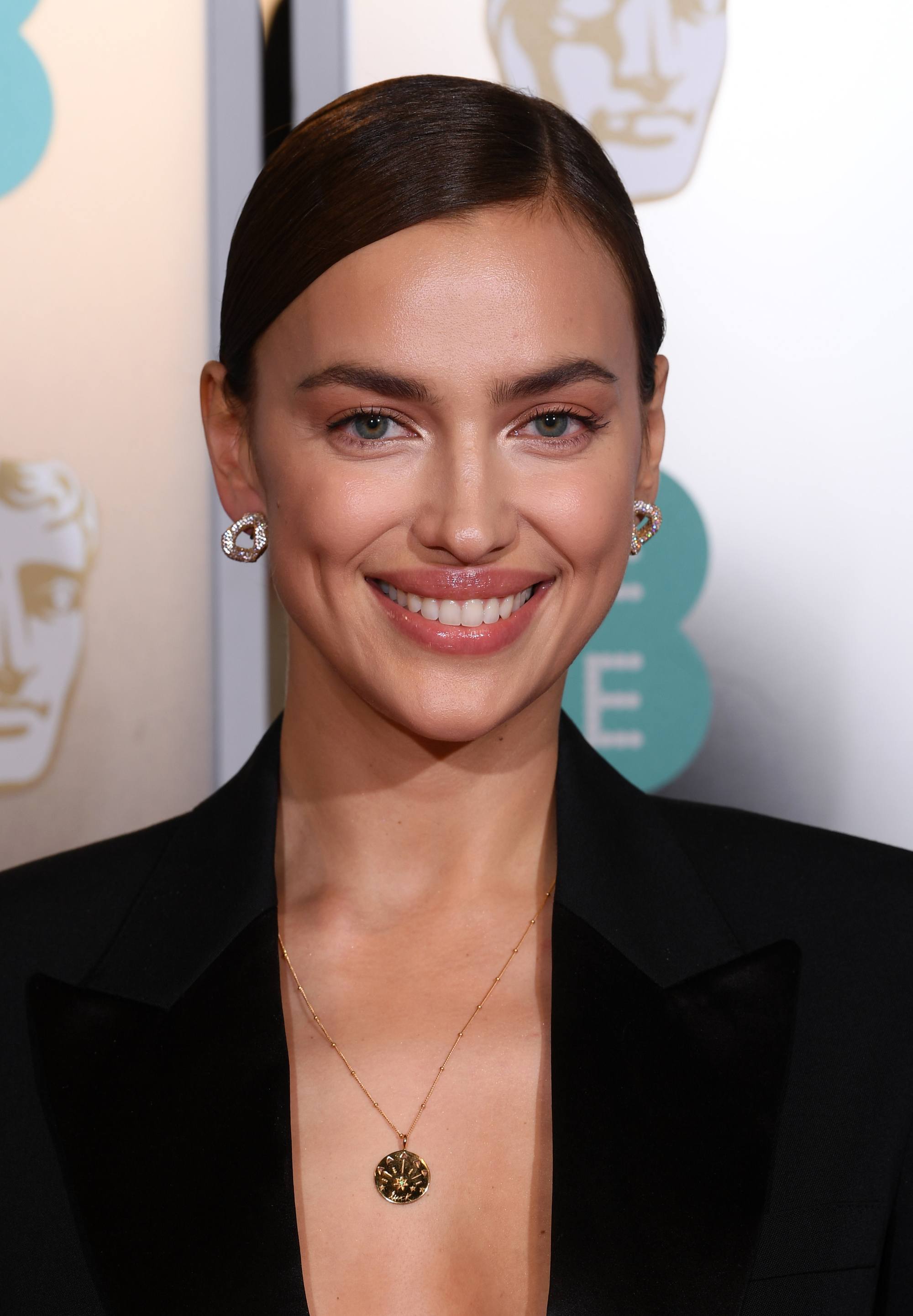 Red carpet hairstyles: Irina Shayk with brown hair styled in side parted smooth bun updo wearing a black smart jacket.
