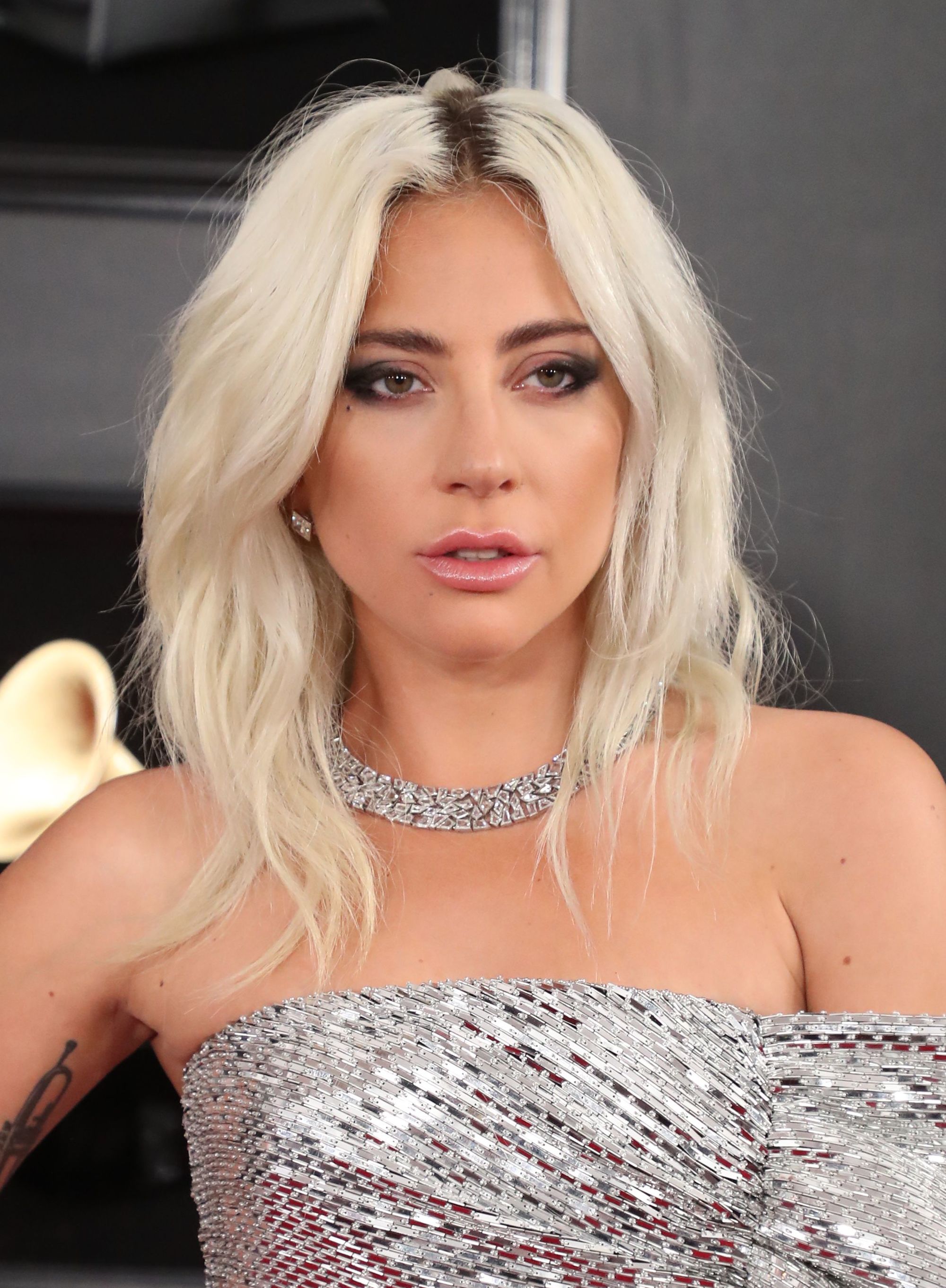 Red carpet hairstyles: Lady Gaga with platinum blonde wavy medium length hair with dark roots wearing a silver dress at the Grammy awards 2019.