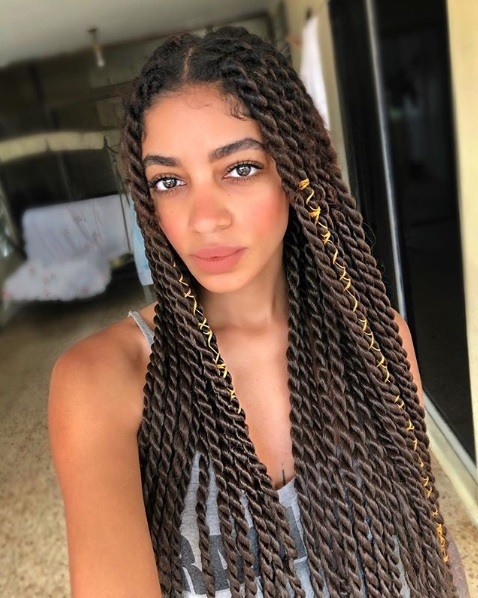 Woman with very long chocolate brown box twists parted in a centre parting with yellow gold yarn wrapped around them