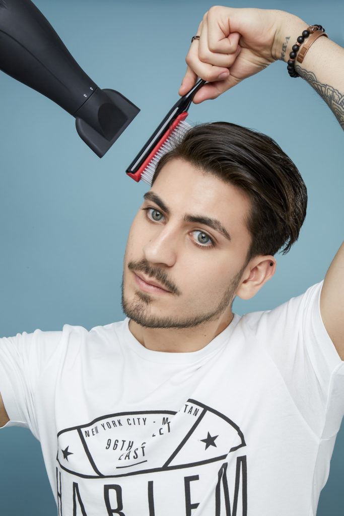 How to blow dry men's hair: Brown haired man with hair swept to one side using a plastic brush to dry his hair