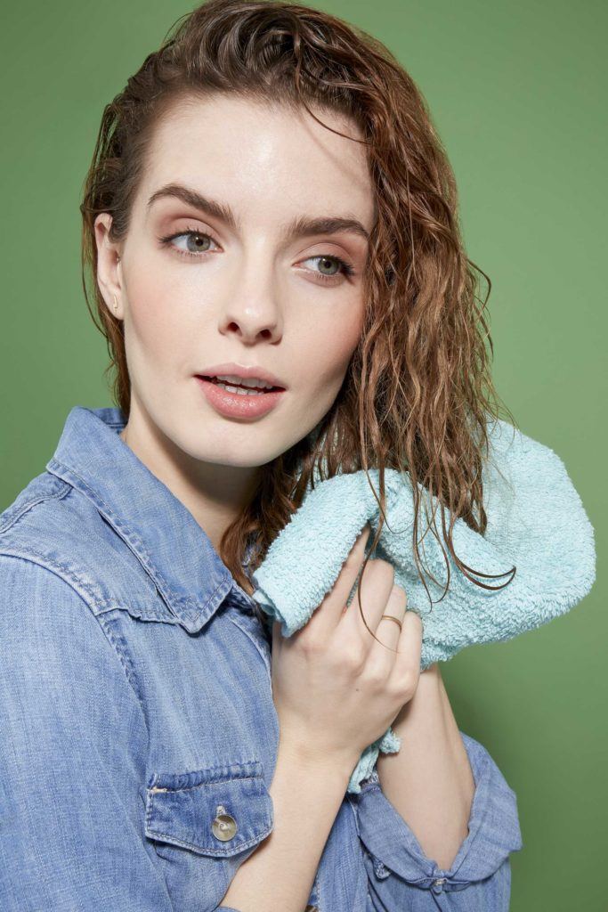 How to scrunch hair tutorial: Close up of a woman with curly brown hair which she is drying with a blue microfibre towel
