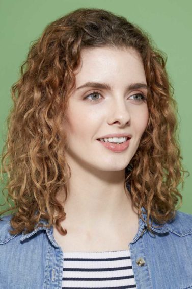 How to scrunch hair tutorial: Woman with brown curly shoulder length hair wearing a striped top and denim shirt