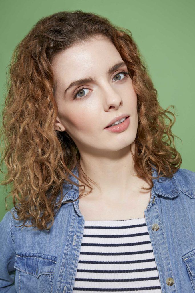 How to scrunch hair tutorial: Close up of a woman with shoulder length scrunched curly hair wearing a striped top and a denim shirt