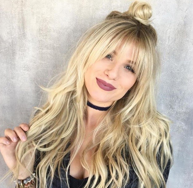 Long shag haircut: Close up shot of a woman with golden blonde long shag hairstyle, wearing a black top and choker in a studio setting