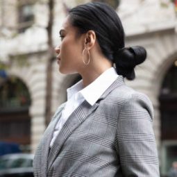 Knot bun hairstyle: Close up shot of a woman with a dark low knot bun wearing checked jacket with white top, wearing belt bag and posing on the street