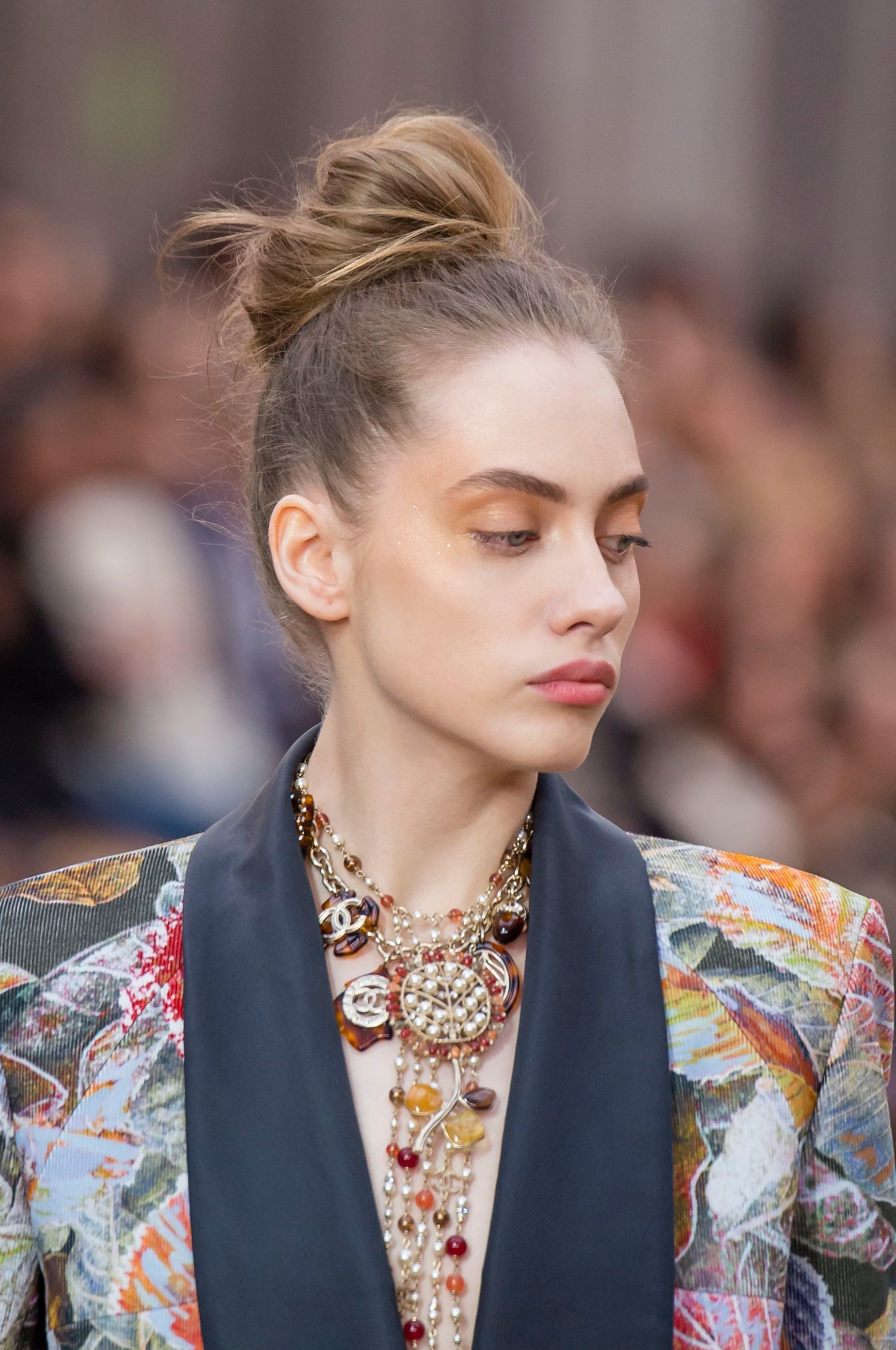 Knot bun hairstyle: Runway picture of a woman with light brunette hair in a loose messy top knot