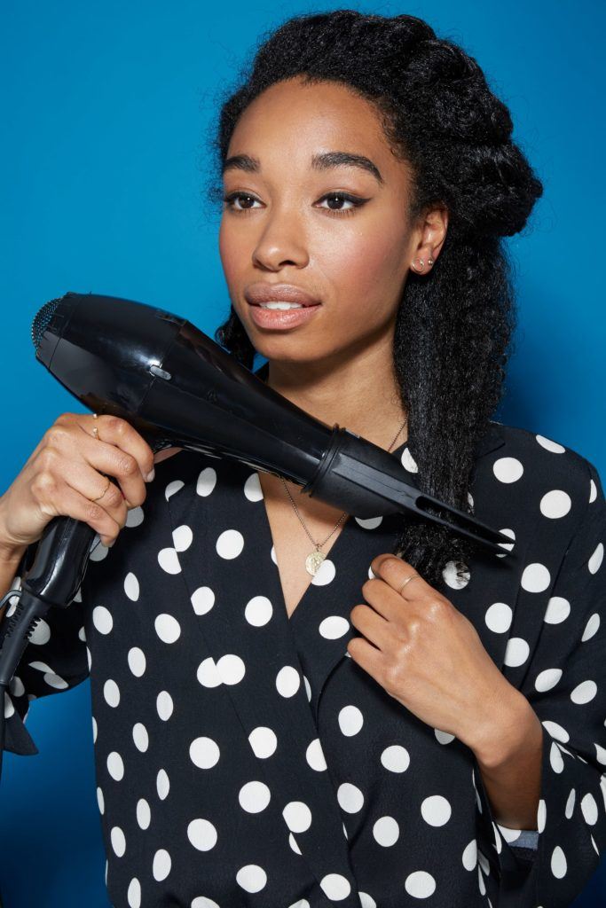 Blow out natural hair: Woman with dark brown natural hair using a hairdryer and pik attachment to blow dry her hair straight