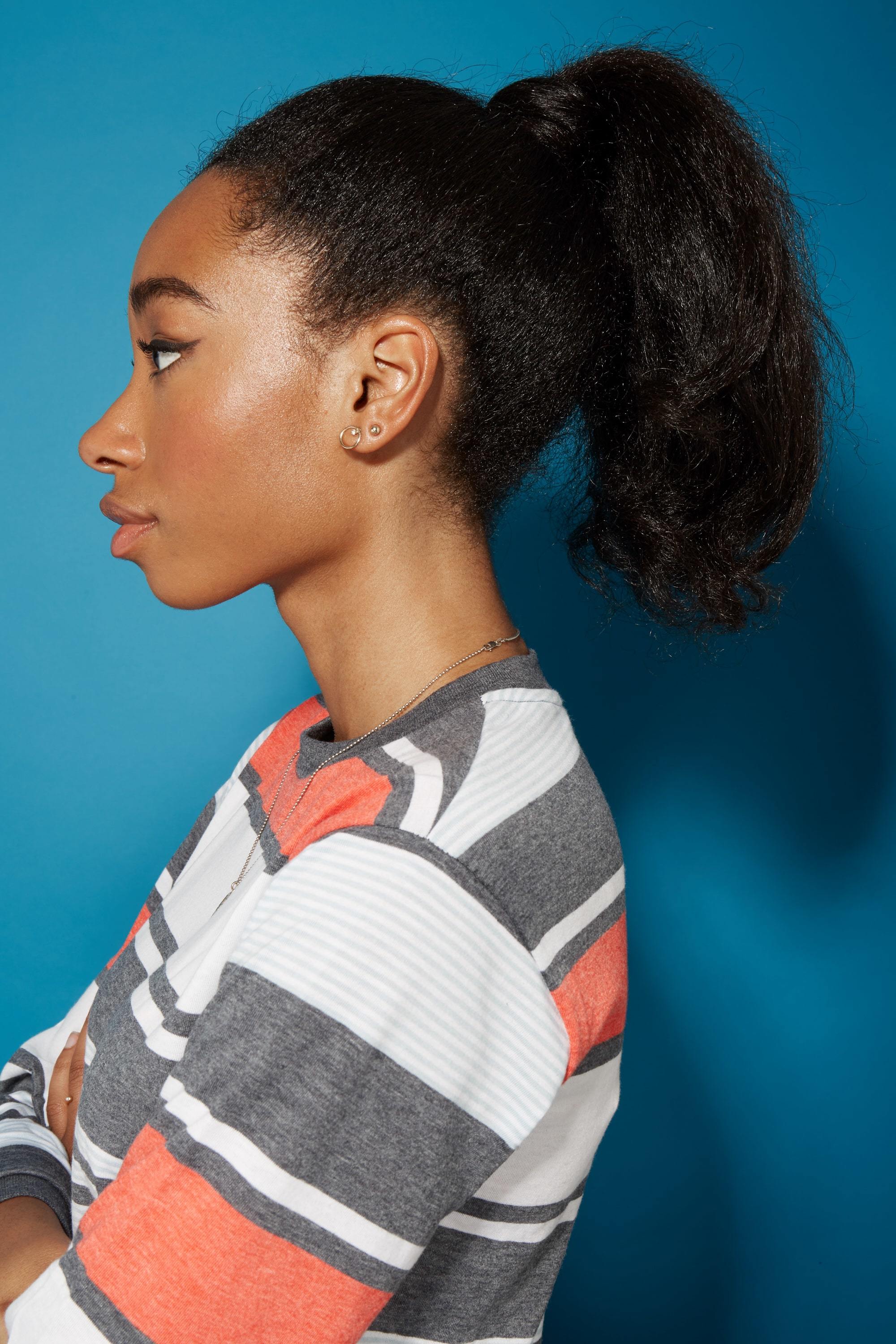 Blow out natural hair: Side profile of a woman with straightened natural hair in a high wrapped ponytail wearing a striped top.