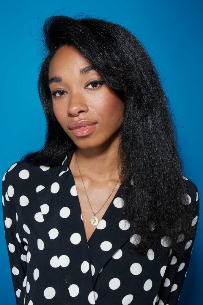 Blow out natural hair: Close-up of a woman with straightened dark brown natural hair with a sweeping side fringe, wearing a black and white polka dot shirt.