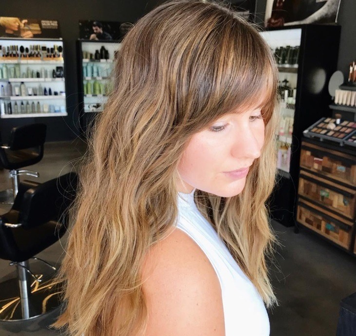 Long shag haircut: Close up shot of a woman with light brown hair with low lights, wearing a white top and posing in a studio setting