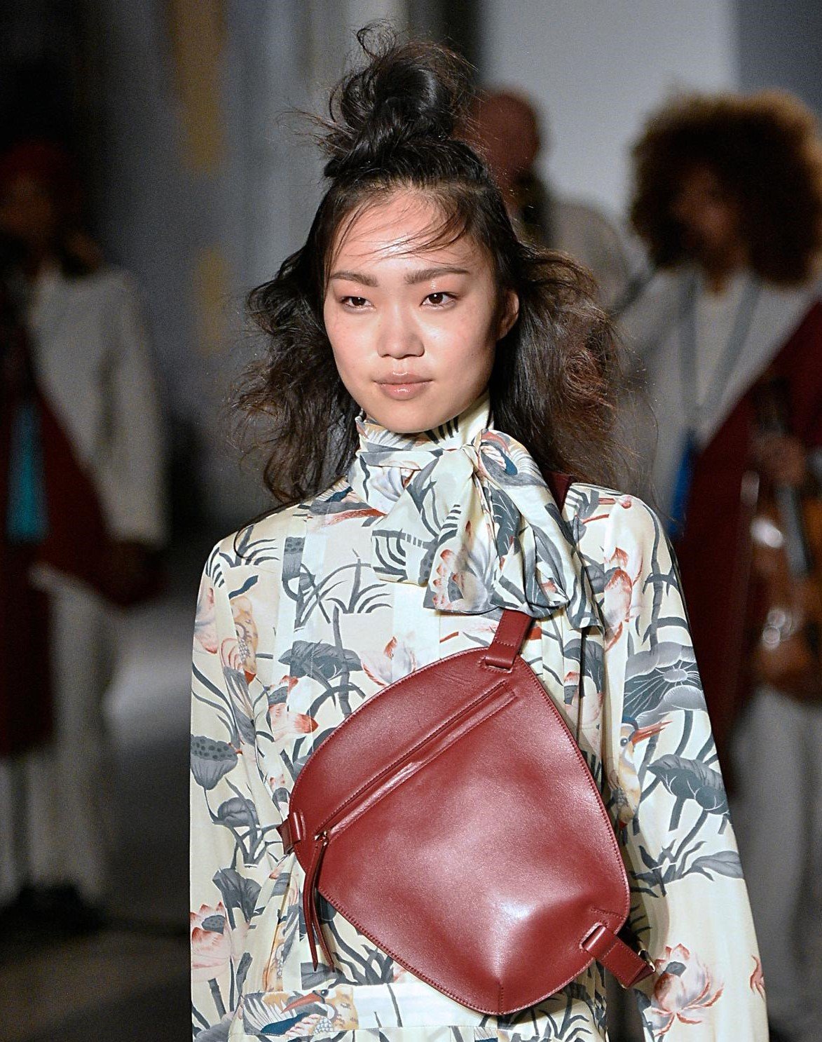 Knot bun hairstyle: Runway picture of a woman with dark brown shoulder length wavy hair in a half-up half-down top knot hairsyle