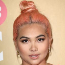 2019 hair colour trends: Hayley Kiyoko with orangey peach hair worn in a top knot, wearing a red dress and necklaces