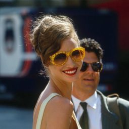 Christy Turlington with brown hair in side parted updo wearing yellow sunglasses and yellow dress.