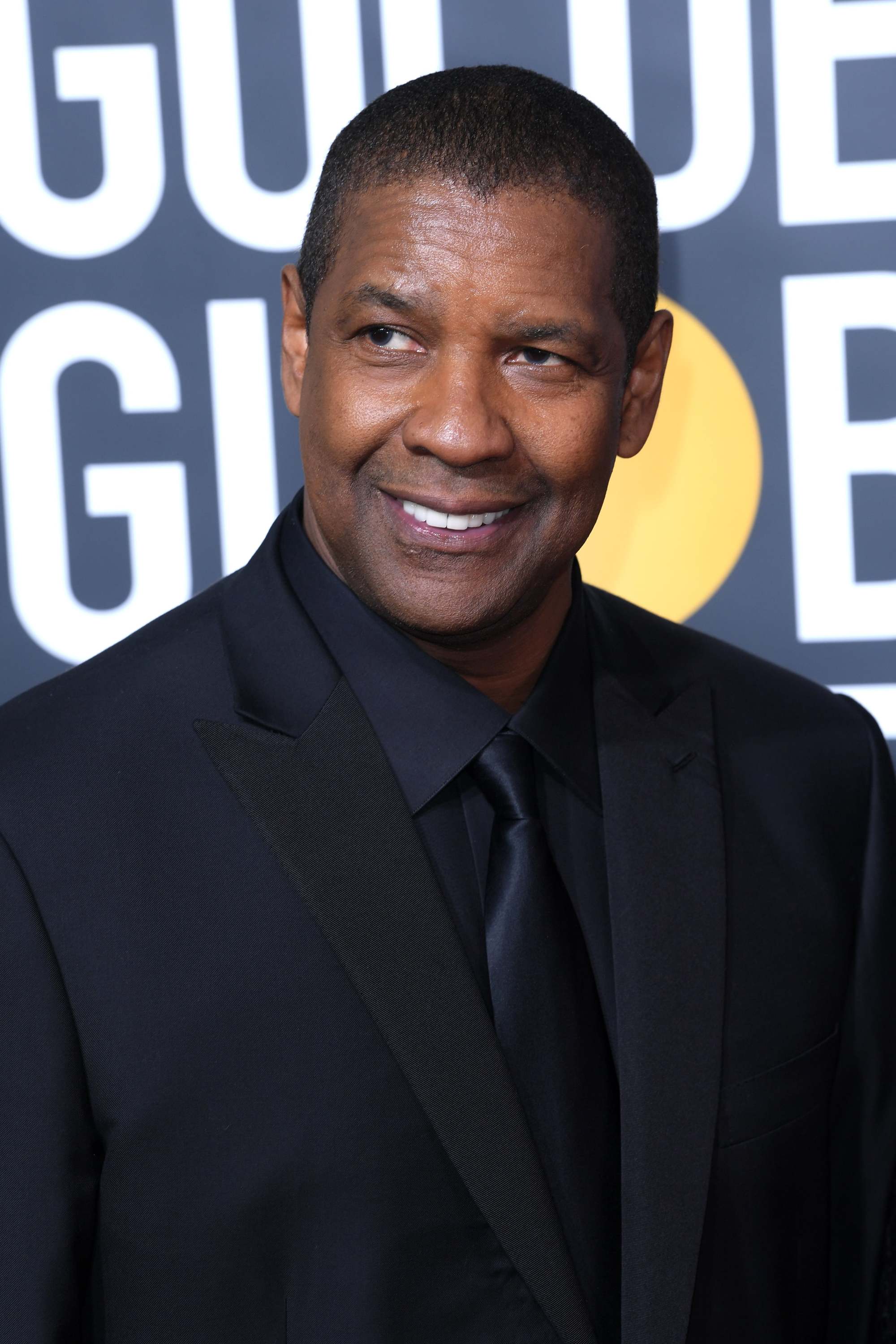 Hairstyles for men over 50: Denzel Washington with short shaved hair wearing a black suit at Golden Globes event.