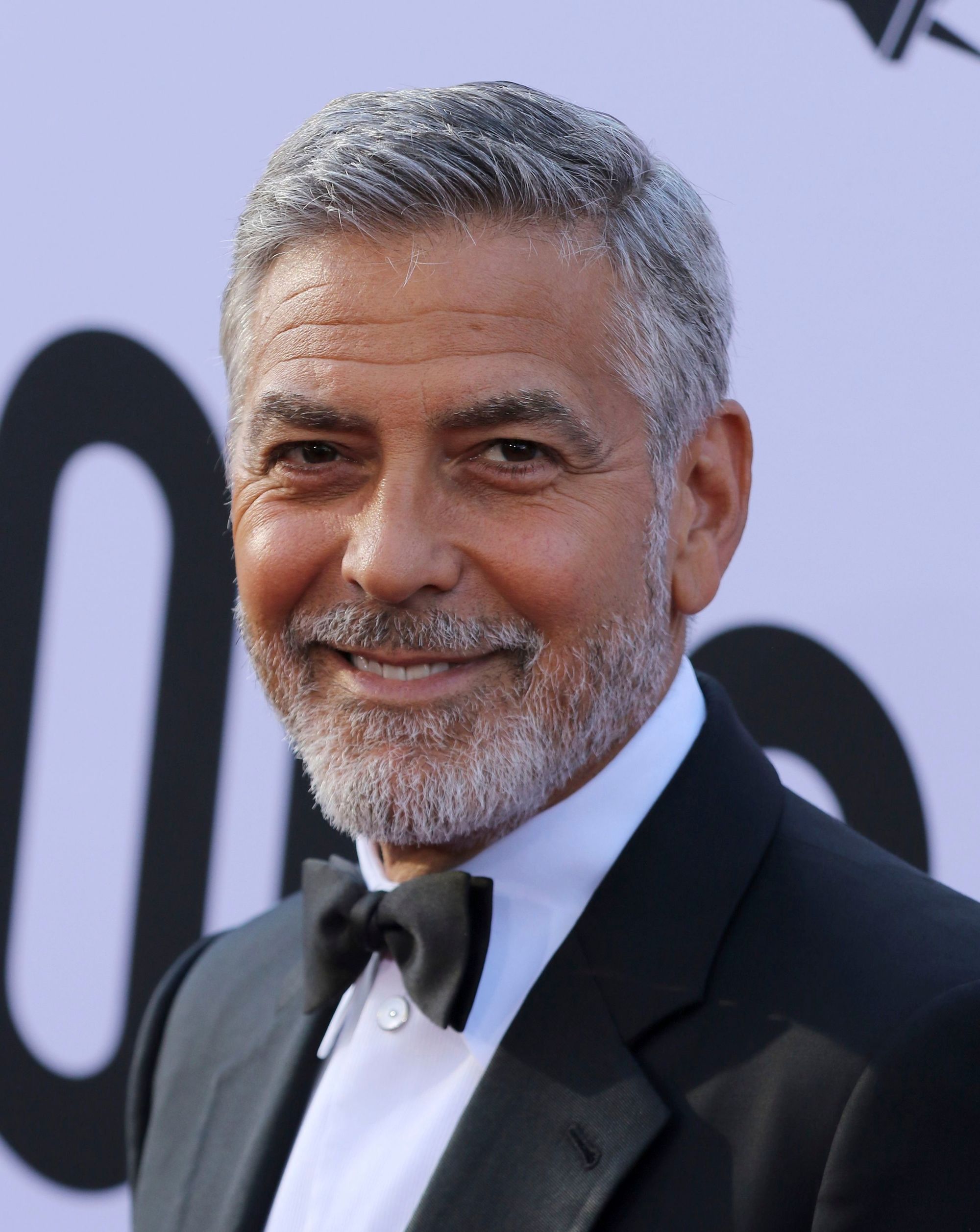 Hairstyles for men over 50: George Clooney with a short tapered combover and grey beard wearing a smart suit.