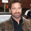 Hairstyles for men over 40: Gerard Butler with short curly brown hair and stubbly facial hair,wearing a shirt and a brown leather jacket