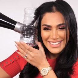 Viral water bottle and hair curling hack: Huda Kattan using a water bottle and hair dryer to curl her hair, wearing red and posing in a studio