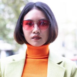 Turtleneck hair ideas: Woman with chocolate brown hair tucked into her orange turtleneck top, wearing mint blazer with sunglasses outside