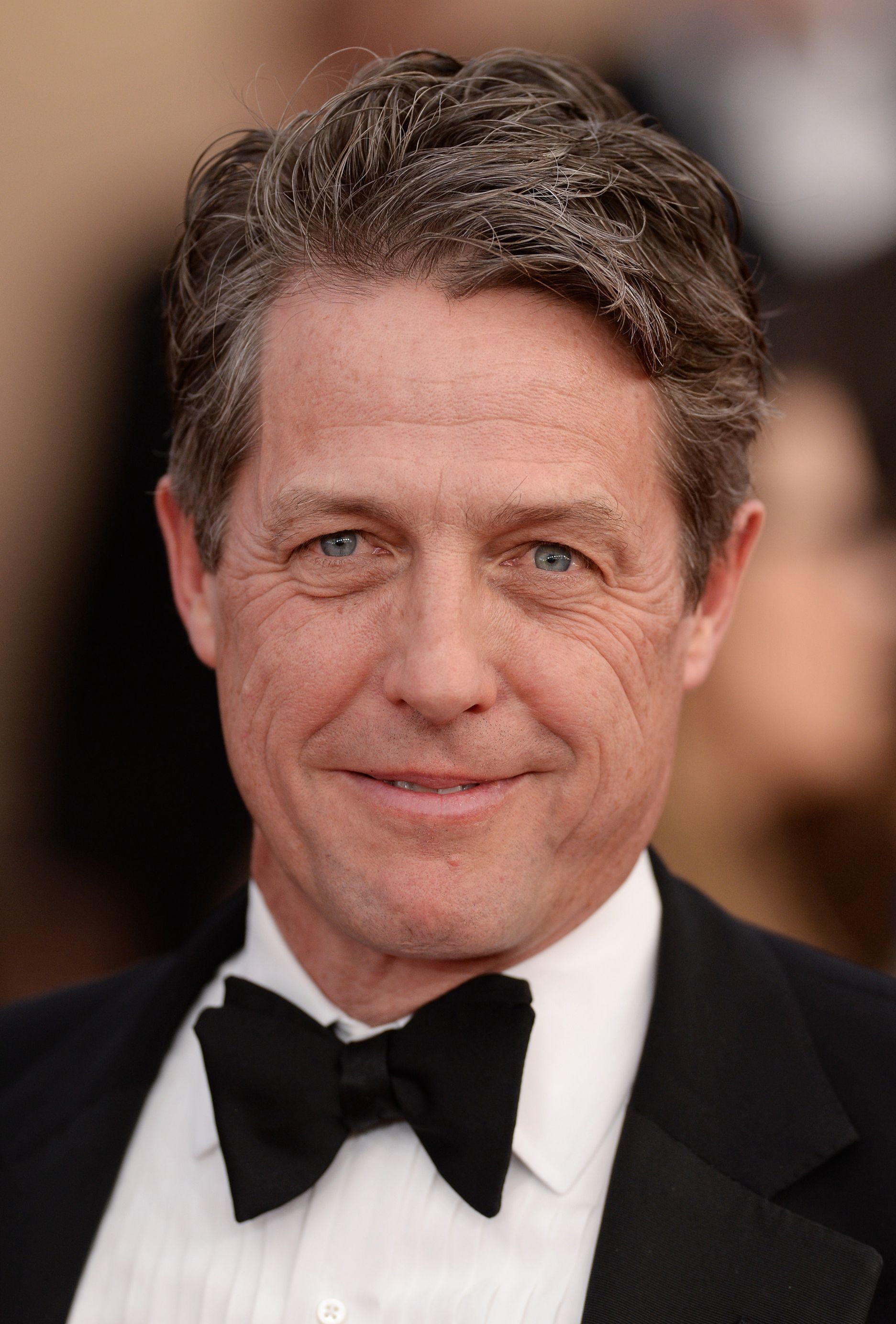 Hairstyles for men over 50: Hugh Grant with light brown textured short hair wearing a formal suit at event.