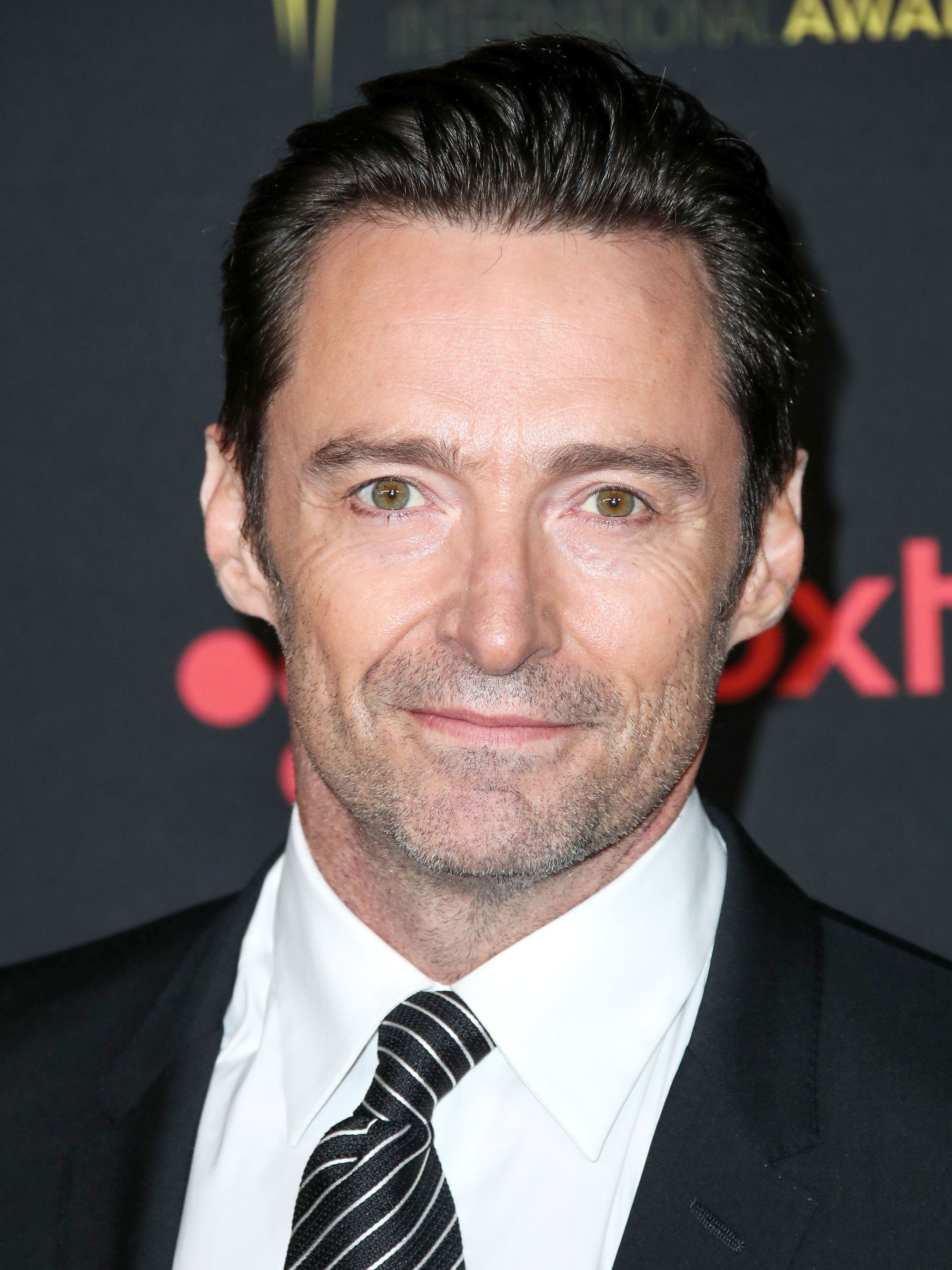 Hairstyles for men over 50: Hugh Jackman with brown swept back short hair wearing a smart suit on the red carpet.