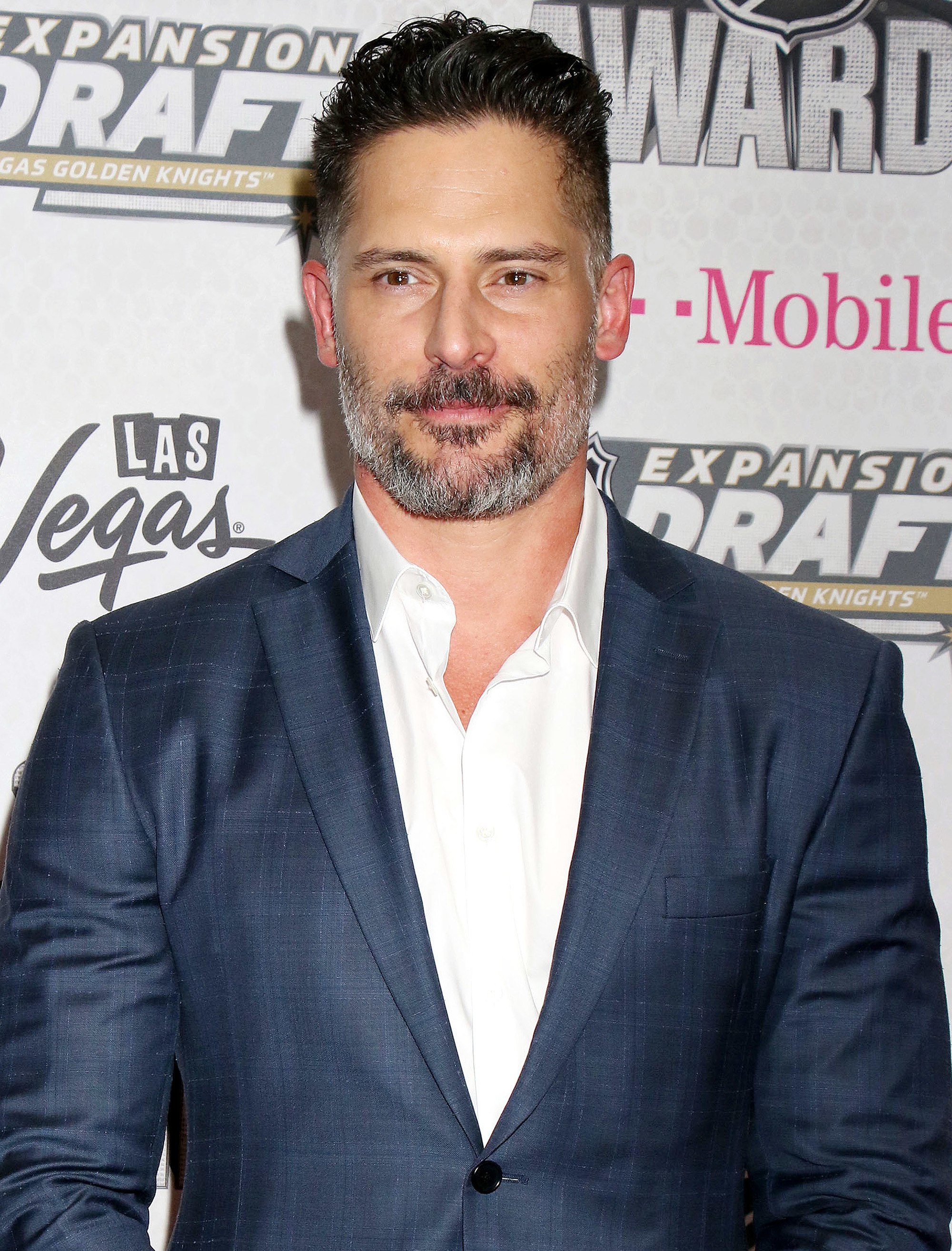 Hairstyles for men over 40: Photo of Joe Manganiello with gelled up brown hair and grey facial hair, wearing a white shirt and blue suit jacket