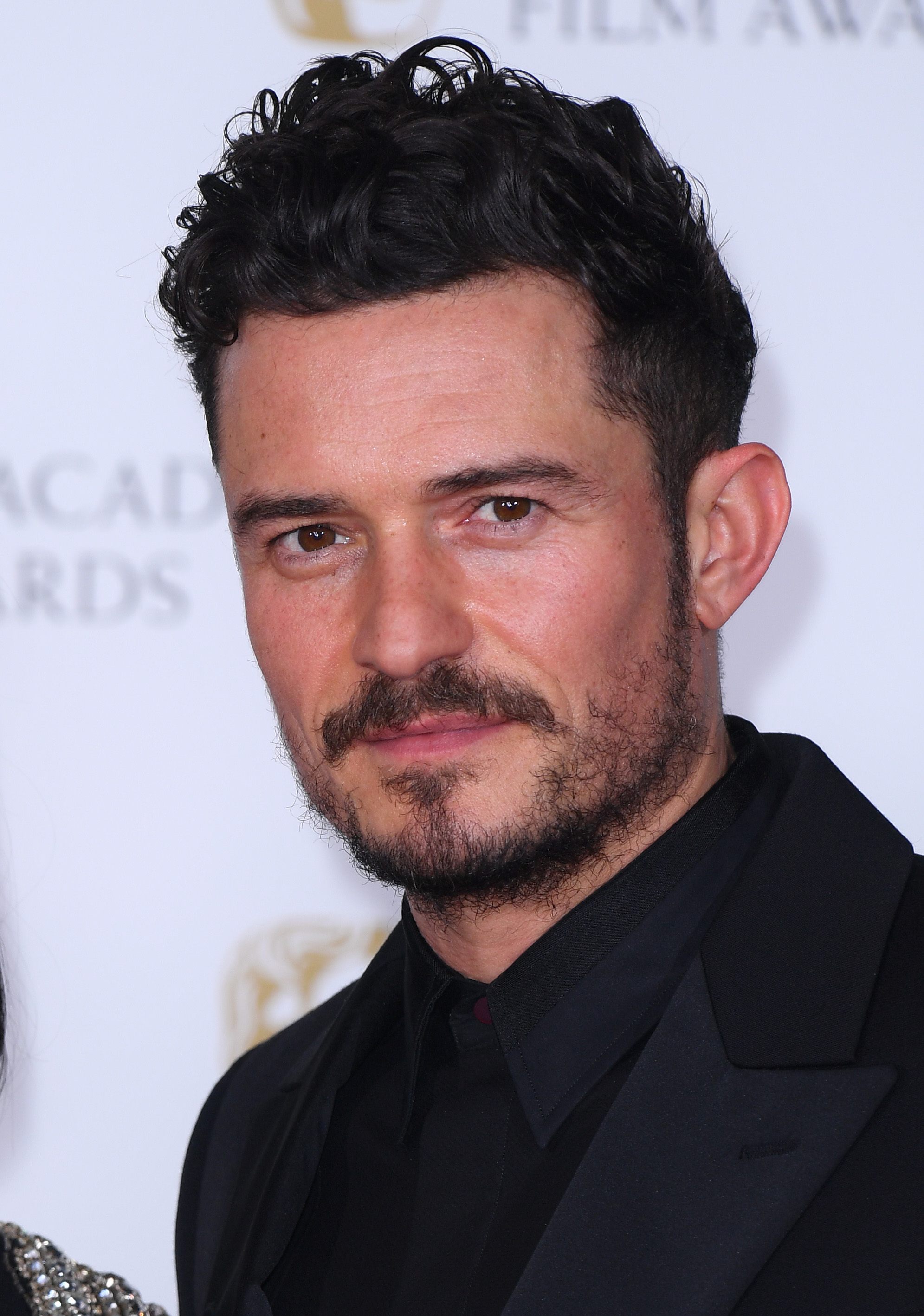 Hairstyles for men over 40: Close-up of Orlando Bloom with curly tousled dark brown short hair