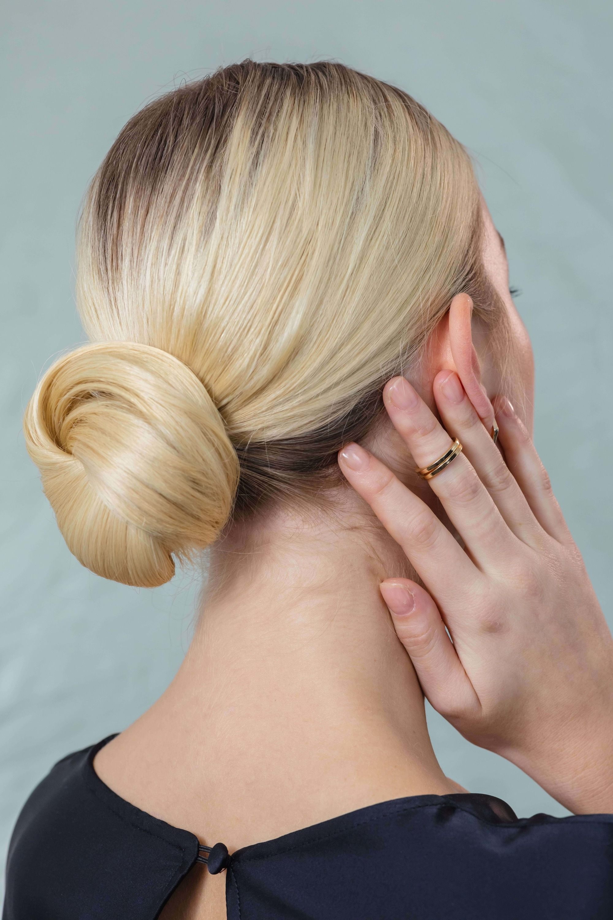 Party hairstyles for medium hair: Woman with straight blonde hair in low chic bun updo wearing a black top.
