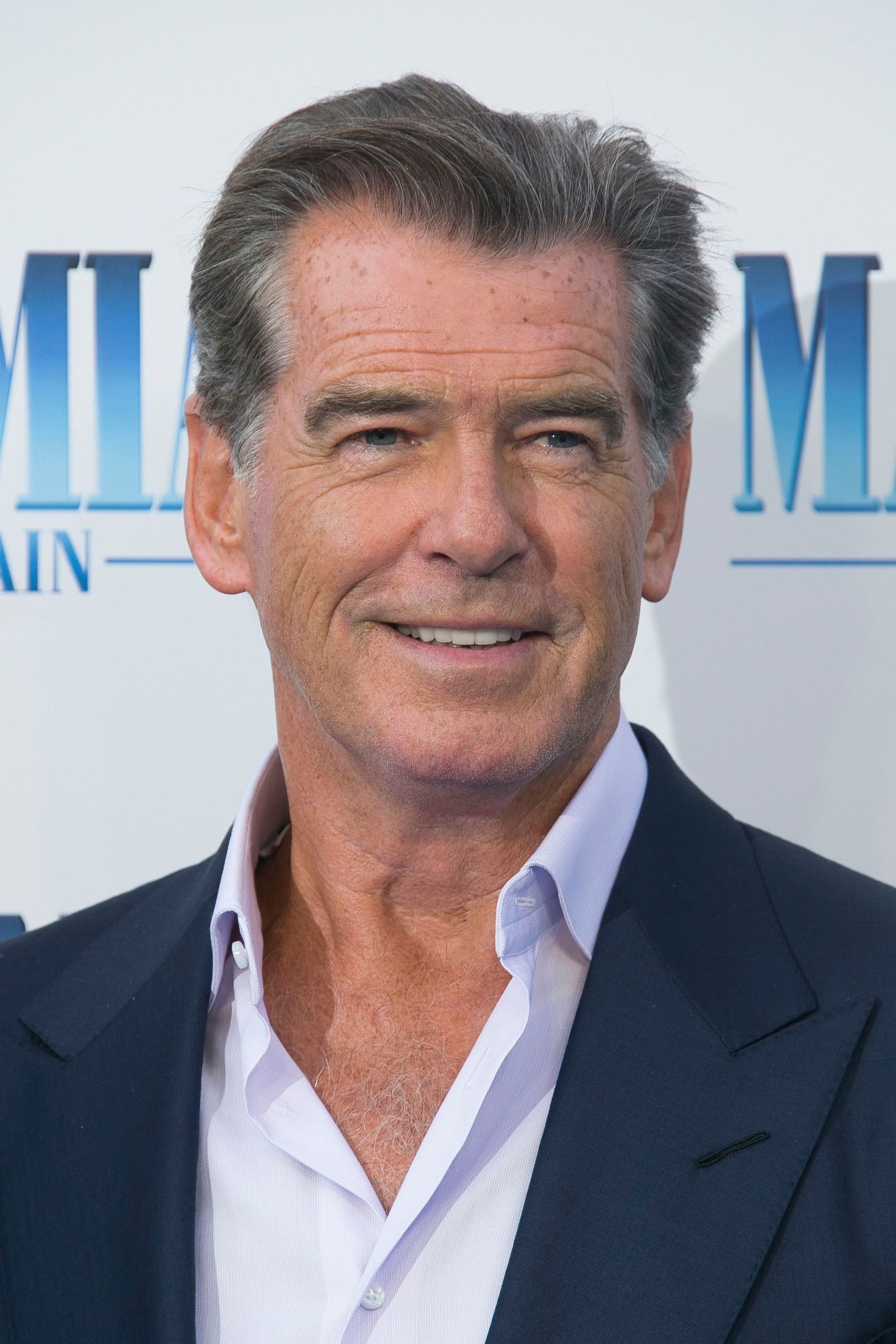 Hairstyles for men over 50: Pierce Brosnan with grey short hair swept back wearing a relaxed blue suit at Mamma Mia premiere.