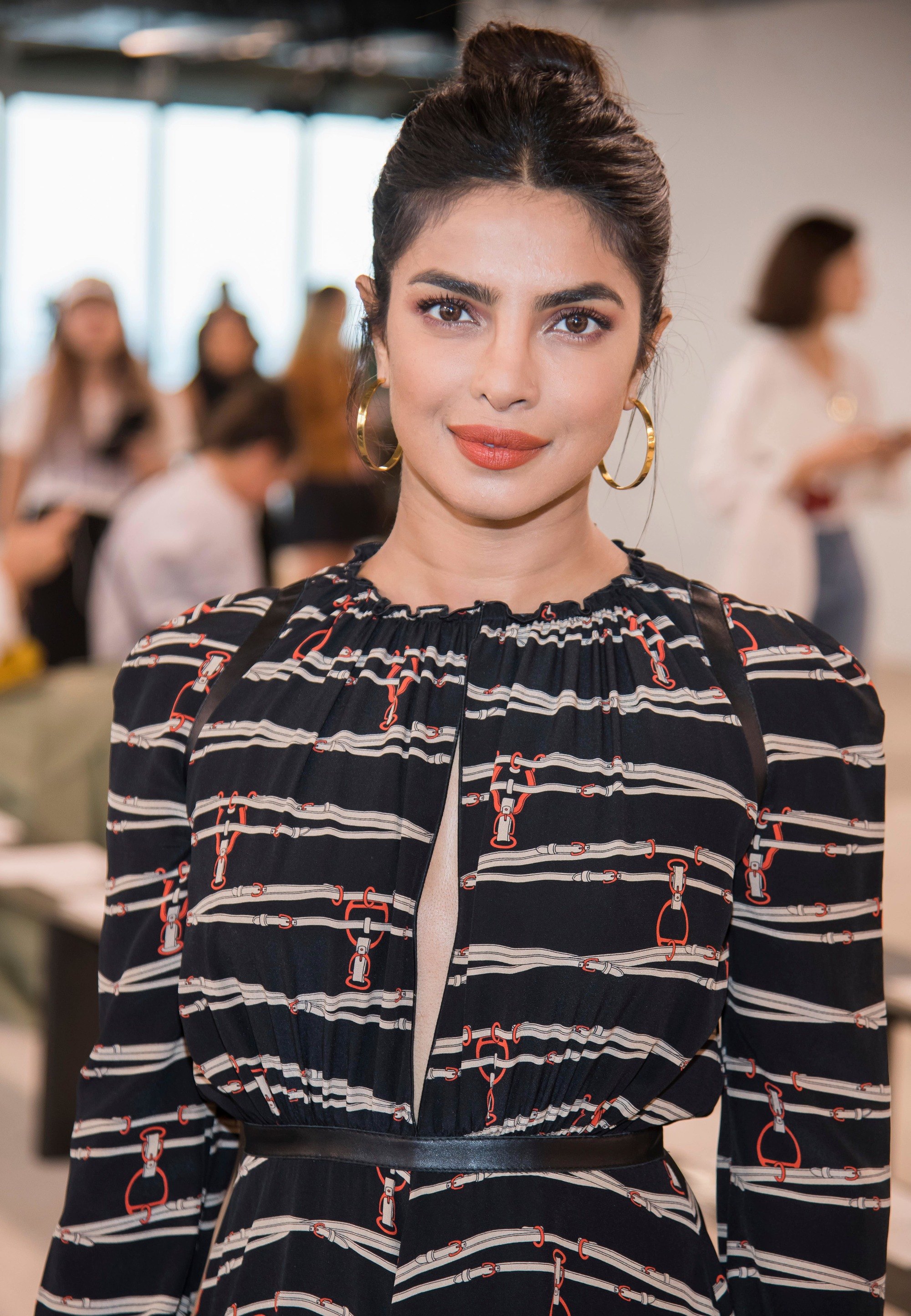Bollywood hair: Priyanka Chopra with dark brown hair styled into a high topknot, wearing hoop earrings and long sleeved dress