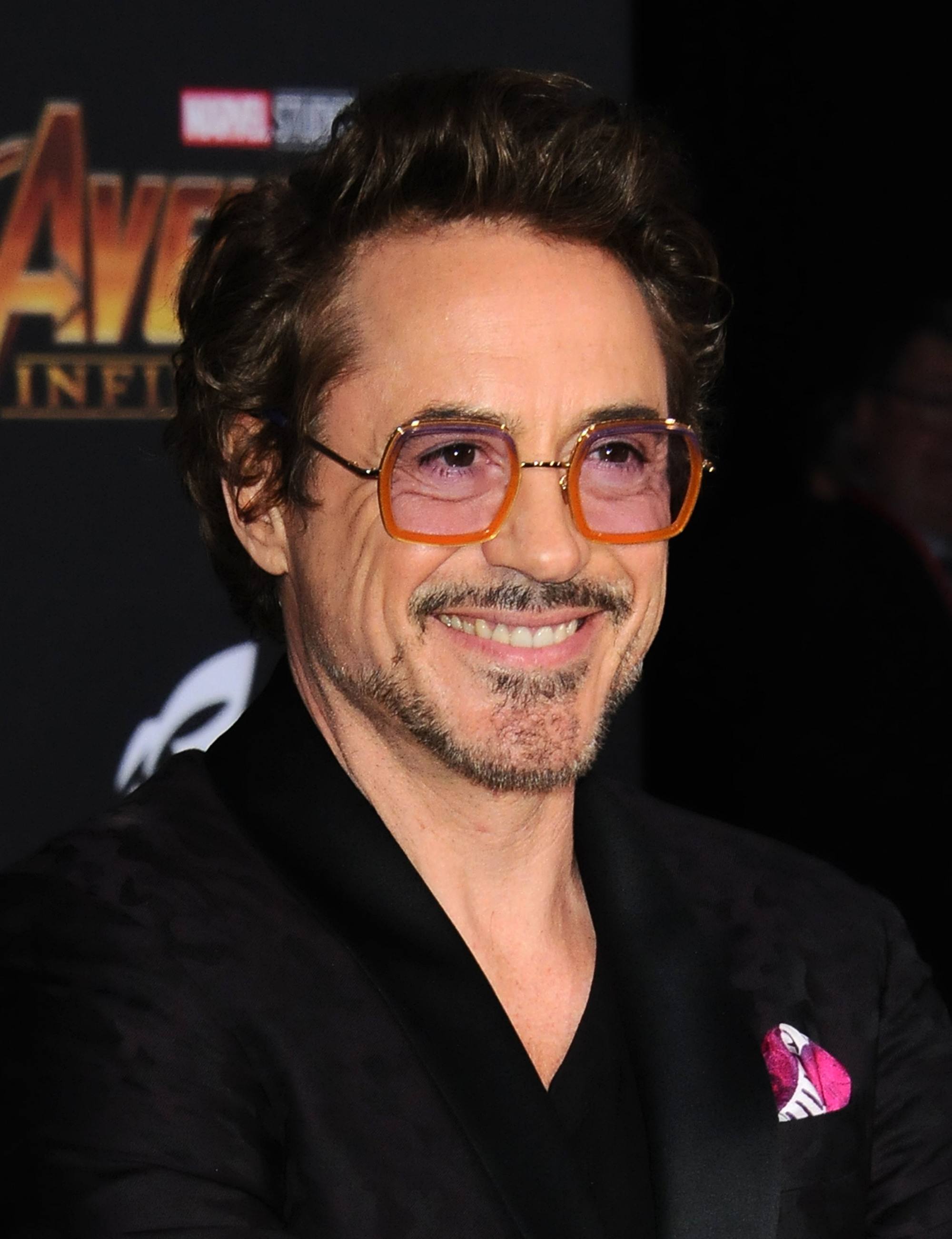 Hairstyles for men over 50: Robert Downey Jr with brown swept back short quiff hair with stubble beard and bold glasses wearing a suit at the Avengers premiere.