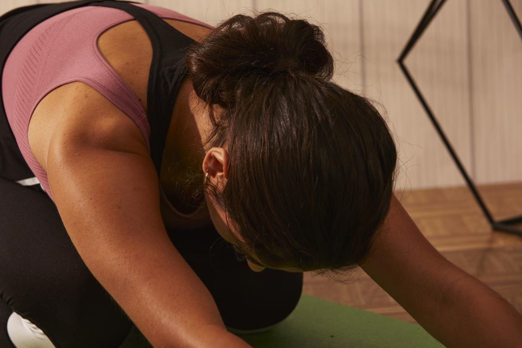 back view of a woman sitting by doing yoga with her brunette hair in a low bun